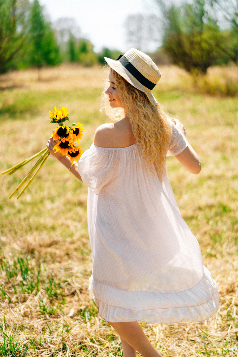 A Woman in White Dress Holding Sunflowers